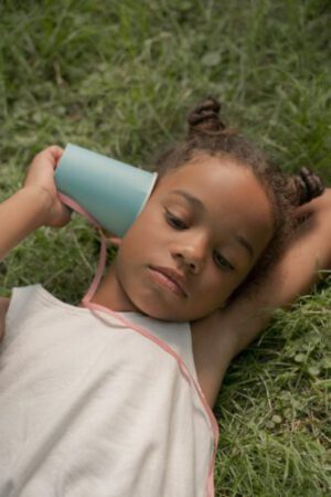 teenage girl laying on grass and holding blue paper cup at ear